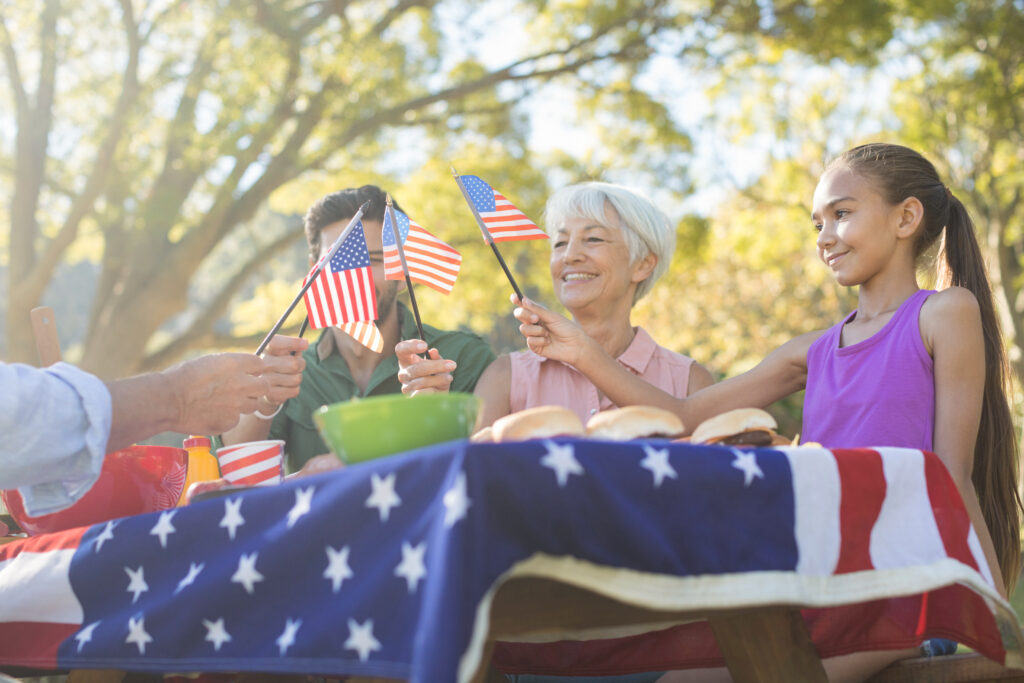 Happy family holding american flags while having meal in the park